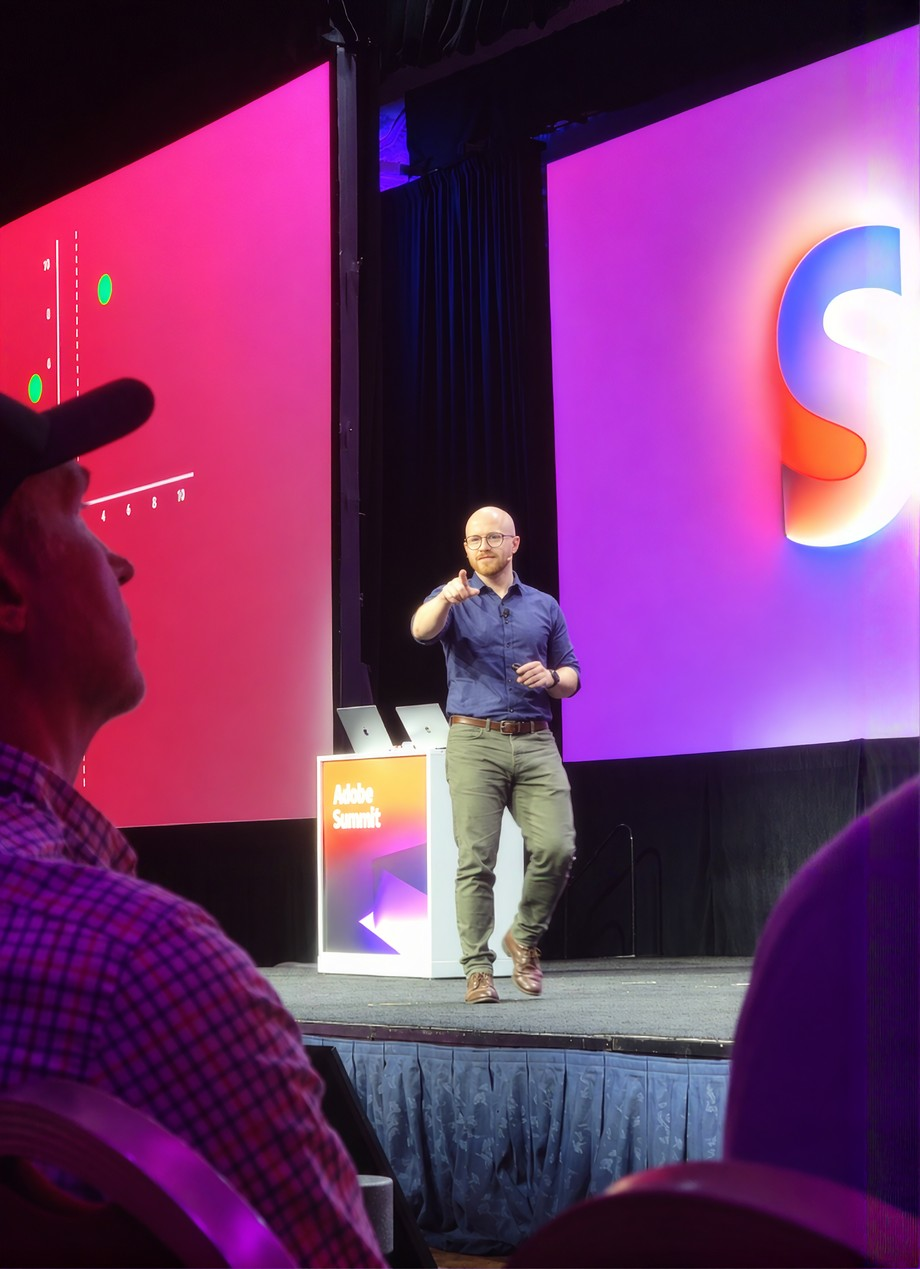 Brendan speaking on stage at Adobe Summit, microphone in hand, mid-gesture to the audience.
